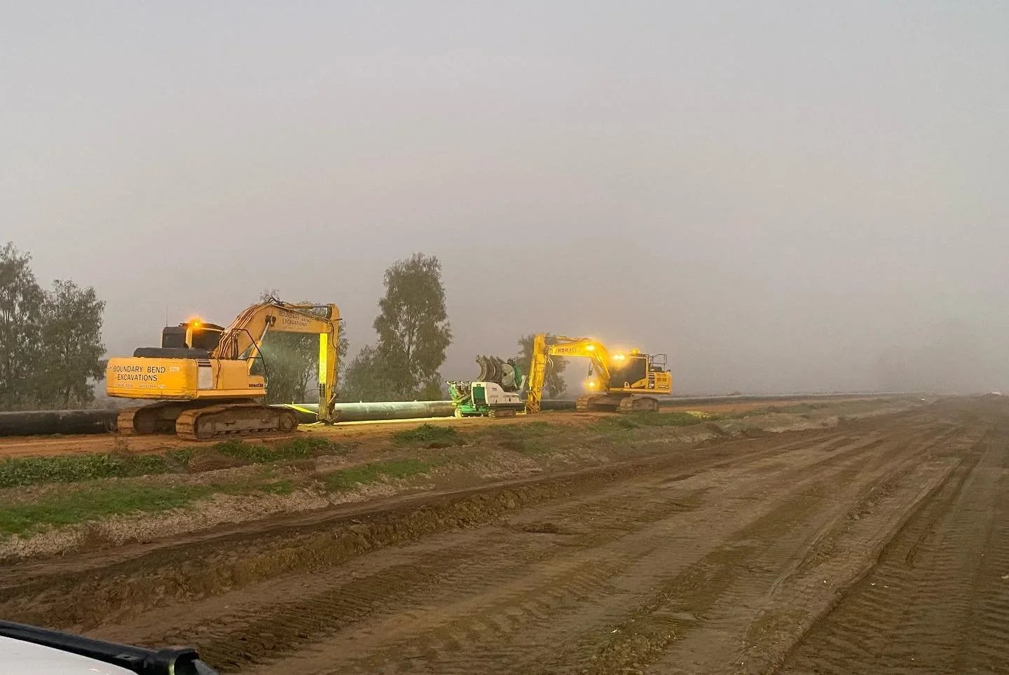 Excavators installing a large poly irrigation pipeline in foggy field conditions